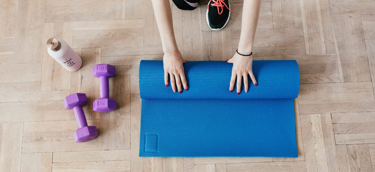hands roll up a yoga mat next to free weights