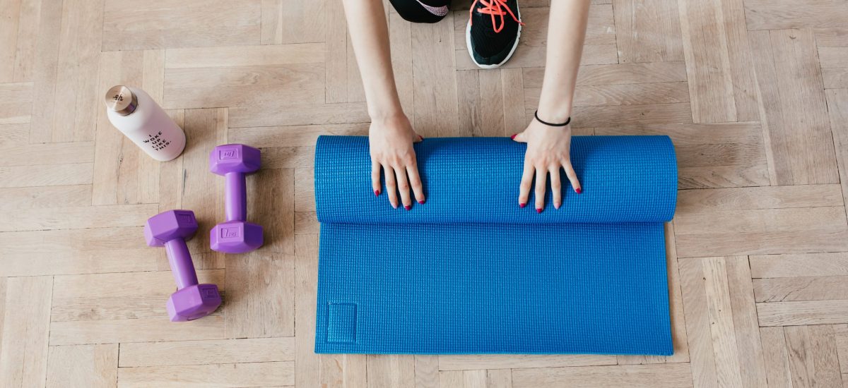 pexels-karolina-grabowska-4498606 hands roll up a yoga mat next to free weights